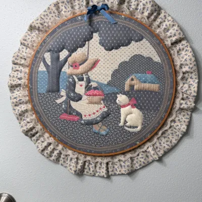 Vintage 1980s handmade country-style fabric applique wall hanging, featuring a Sunbonnet Sue-style girl on a swing with a white cat,...