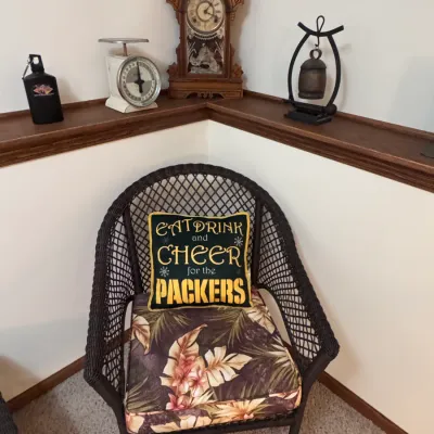 Dark brown wicker armchair with a tropical floral cushion and a Green Bay Packers decorative pillow, shown alongside a vintage kitchen...