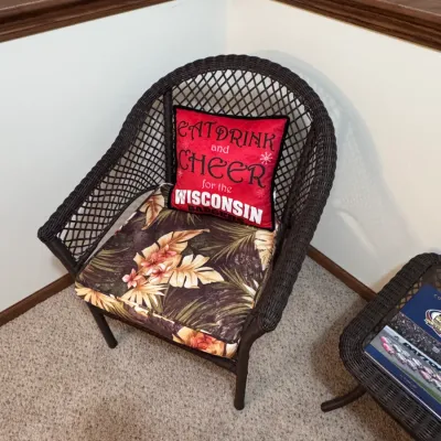 Dark brown resin wicker patio armchair featuring a tropical floral seat cushion and a red Wisconsin Badgers decorative throw pillow.