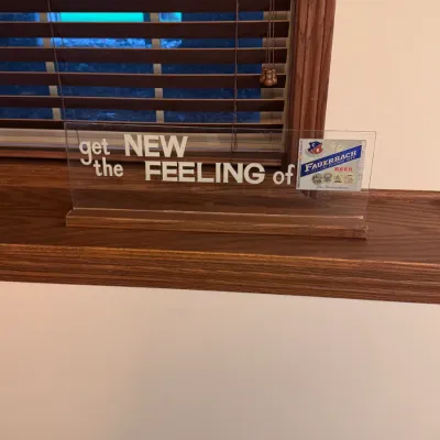 Vintage Fauerbach Beer acrylic counter sign, featuring the slogan "get the NEW FEELING of Fauerbach Beer" on a wooden base,...