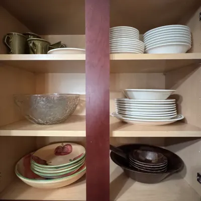 Assorted kitchen dinnerware and serveware, including Corelle white plates and bowls, hand-painted apple motif ceramic bowls, a textured...