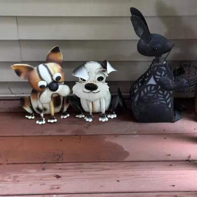 Trio of whimsical metal garden statues, including two cartoonish dogs and a black filigree rabbit, suitable for outdoor lawn or patio decor.