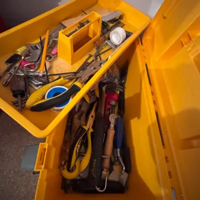 Yellow plastic toolbox with removable top tray, filled with assorted hand tools including an Estwing hammer, pliers, wrenches, and hardware.