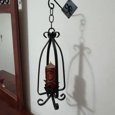 Vintage Spanish Revival wrought iron hanging candle holder with wall-mount bracket, featuring scrollwork details and a pillar candle, in...