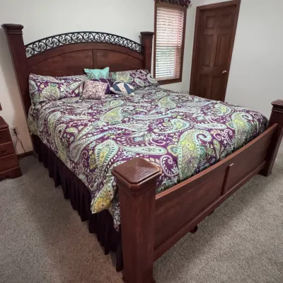 Traditional style wooden king-size bed frame featuring a high arched headboard with decorative black scrollwork metal inlay and thick...