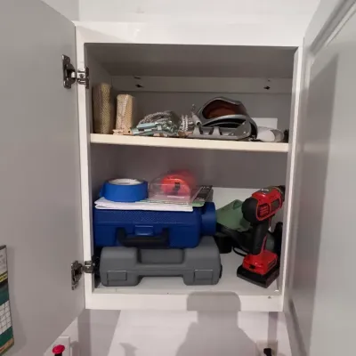 Assorted garage and utility items stored in a white wall cabinet, featuring a red Chicago Electric cordless drill, plastic tool cases,...