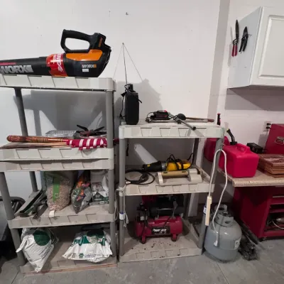 Assorted garage tools and equipment, featuring a Worx cordless leaf blower, a Powermate portable air compressor, and various lawn care...