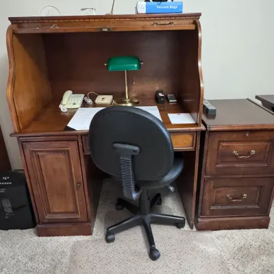 Vintage wooden rolltop desk with a matching two-drawer filing cabinet, paired with a black adjustable office chair and a classic green...