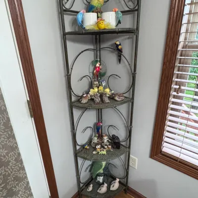 Four-tier metal corner baker's rack featuring decorative scrollwork and woven wire shelves, styled with an assortment of ceramic...