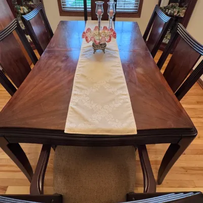 Traditional wooden dining table set featuring a rich mahogany finish, sunburst veneer tabletop pattern, and six matching high-back chairs...