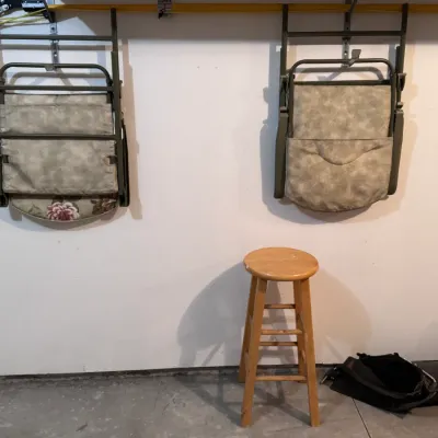 Pair of vintage folding lawn chairs with patterned fabric seats hanging on wall brackets, shown alongside a simple wooden bar stool in a...