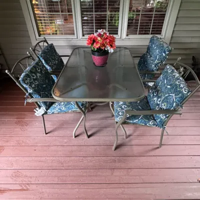 Five-piece outdoor patio dining set featuring a rectangular glass-top table with a metal frame and four matching armchairs outfitted with...