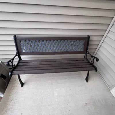 Outdoor garden bench featuring a dark brown wooden slat seat and backrest with a decorative woven-pattern metal insert, supported by a...