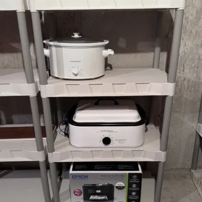 Hamilton Beach slow cooker and 18-quart roaster oven, made in China, displayed on a plastic shelving unit alongside a boxed Epson...
