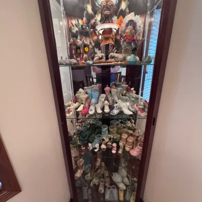Vintage wooden corner curio cabinet with glass shelves and interior lighting, displaying a collection of Native American Kachina dolls...