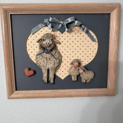 Country-style framed 3D wall art featuring a sheep and lambs motif, set against a heart-patterned background with ribbon accents in a...