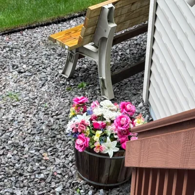 Outdoor wooden garden bench with durable composite supports, paired with a rustic wooden barrel planter filled with vibrant artificial...