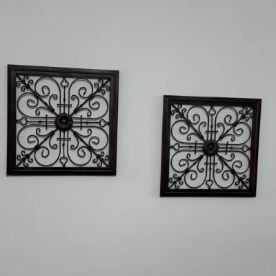 Pair of square wrought iron wall art plaques featuring intricate scrollwork and a central floral motif, set within dark wood frames.