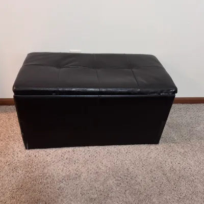 Contemporary black faux-leather storage ottoman bench featuring a tufted hinged lid, ideal for living room seating or bedroom storage.