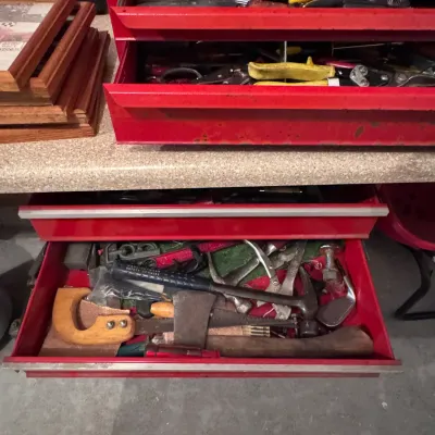 Vintage red metal Craftsman tool chest with multiple drawers containing an assortment of hand tools, including a hammer, hand saw, and...