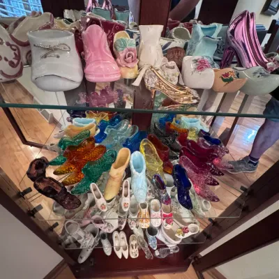 Large collection of vintage collectible shoe figurines, featuring Fenton art glass slippers, porcelain baby booties, and ceramic high...