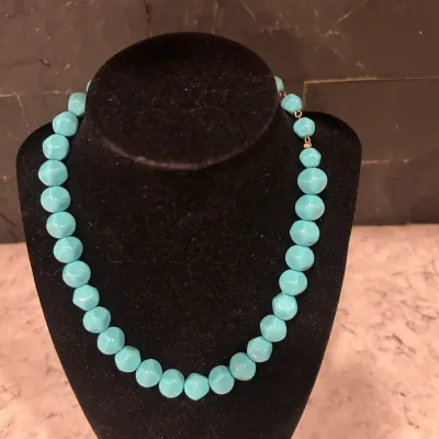 Vintage turquoise-colored molded plastic bead necklace on a black velvet display stand.