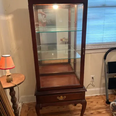 Traditional cherry wood curio cabinet featuring glass shelves, a mirrored back, interior lighting, and a single drawer base with cabriole...