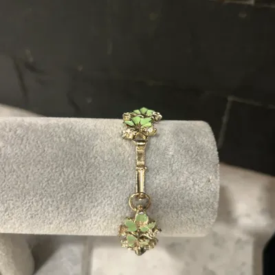 Vintage gold-tone bracelet featuring light green enamel floral details, displayed on a grey velvet jewelry stand.