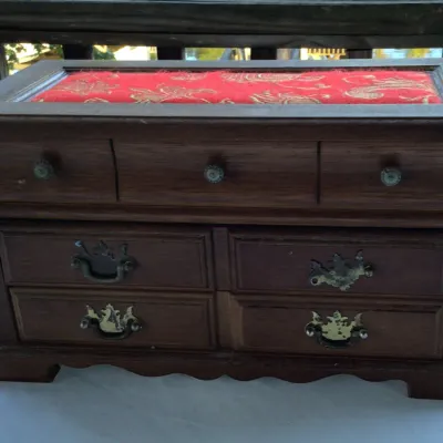 Vintage wooden jewelry chest featuring a red brocade fabric top insert, three small upper drawers, and four larger lower drawers with...