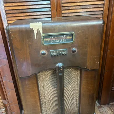 Vintage Philco floor console radio in a wooden cabinet, showing some veneer damage on the top left corner.
