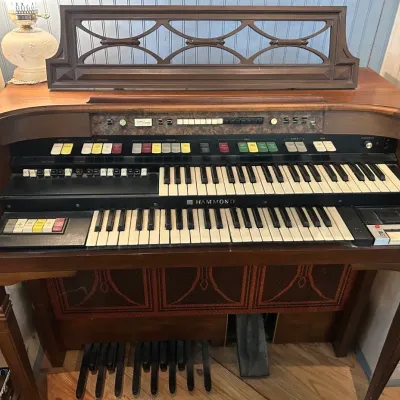 Vintage Hammond electronic organ in a wooden cabinet, featuring dual keyboards, foot pedals, and an ornate music stand.