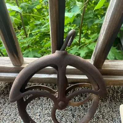 Vintage cast iron well pulley with a heavily rusted patina and integrated hanging hook.