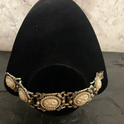 Vintage gold-tone panel link bracelet featuring molded faux pearl cameos with seed bead borders, displayed on a black velvet stand.