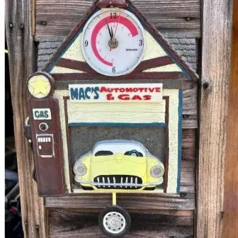 Vintage-style novelty wall clock shaped like a gas station garage, featuring a yellow Corvette-style car, a gas pump, and a tire pendulum.