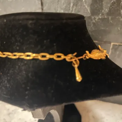 Vintage gold-tone link chain necklace with a decorative drop charm, displayed on a black velvet neck stand.