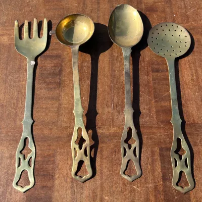 Four-piece vintage brass serving set, including a serving fork, ladle, solid spoon, and slotted spoon, featuring decorative cutout handles.