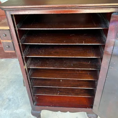 Vintage mahogany sheet music cabinet featuring a single door opening to reveal multiple thin shelves, supported by ball-and-claw feet.