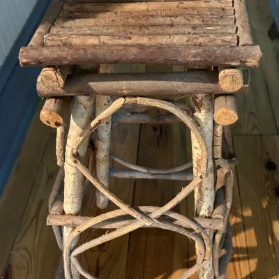 Rustic Adirondack-style twig plant stand or small side table, featuring a slatted branch top and decorative bentwood twig accents.