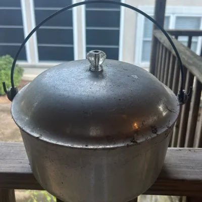 Vintage Guardian Service cast aluminum Dutch oven with a domed lid, glass knob, and wire bail handle, showing signs of heavy use.