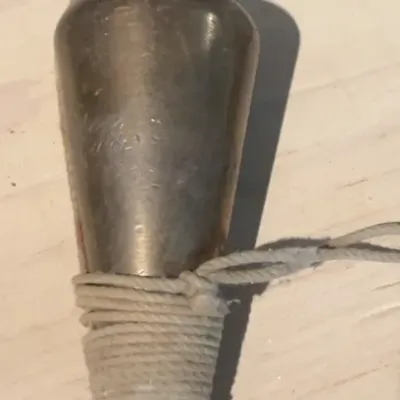 Vintage brass plumb bob with a steel tip and wrapped string, showing a weathered patina from age and use.