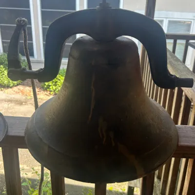 Antique cast iron farm bell with yoke and pull arm, showing a weathered patina and rustic charm.