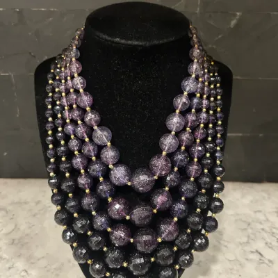 Multi-strand statement necklace featuring graduated purple and black faceted beads with gold-tone spacer beads, displayed on a black...