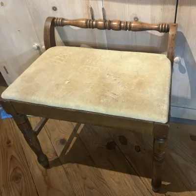 Vintage wooden vanity bench with a spindle backrest, turned legs, and a padded beige velvet seat showing some wear.