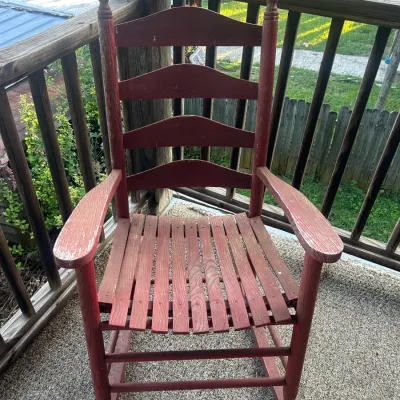 Vintage wooden rocking chair with a red finish, featuring a ladder-back design, slatted seat, and finial-topped posts.