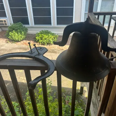 Vintage cast iron farm bell with mounting bracket, showing a weathered dark patina.