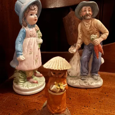 Three vintage porcelain and resin figurines, including a young girl in a bonnet, a farmer holding carrots, and a small figure labeled...