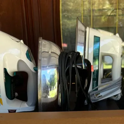 Assorted household irons, including a Black & Decker Pro Finish model, a Rowenta iron, and others, shown in used condition.