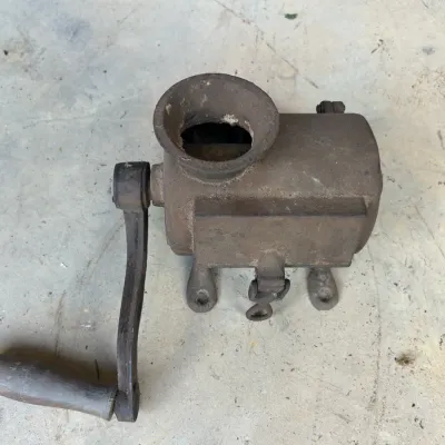 Antique cast iron hand-crank meat grinder with a wooden handle, showing significant rust and patina.