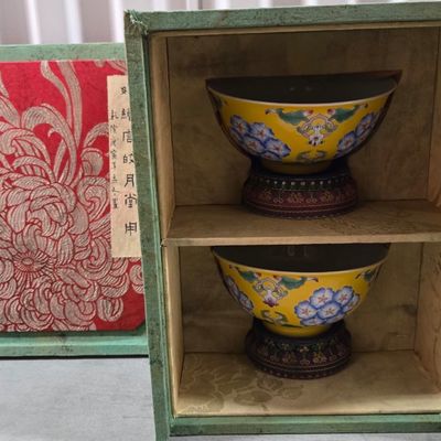 Pair of Chinese yellow-ground porcelain bowls with floral motifs, displayed on wooden stands inside a fabric-lined presentation box with...