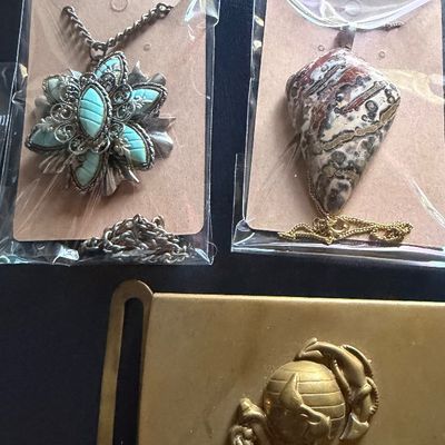 Two packaged pendant necklaces, one featuring a turquoise-colored floral design and the other a polished jasper stone, displayed...